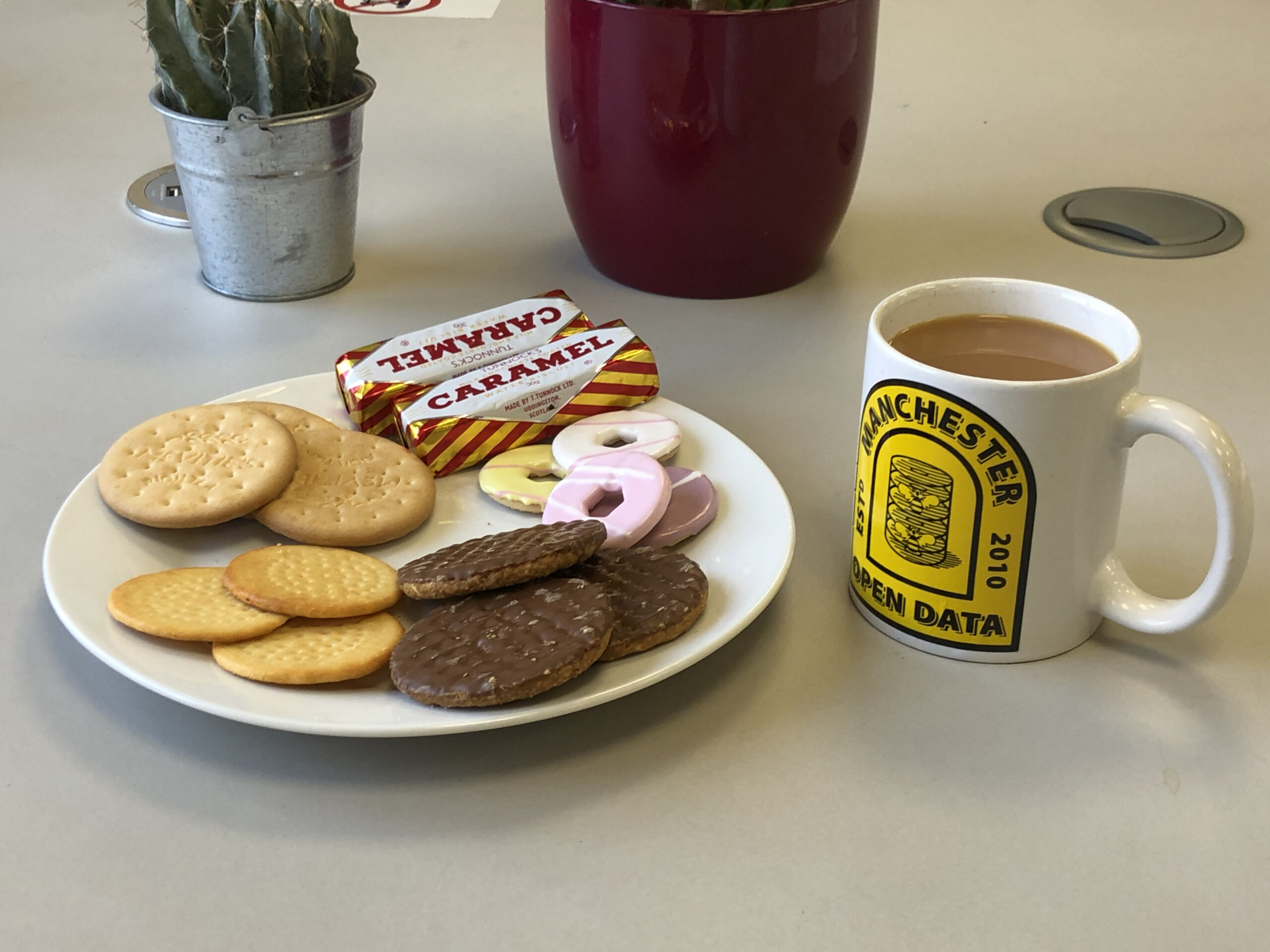 A plate of biscuits and a cup of tea on a desk.