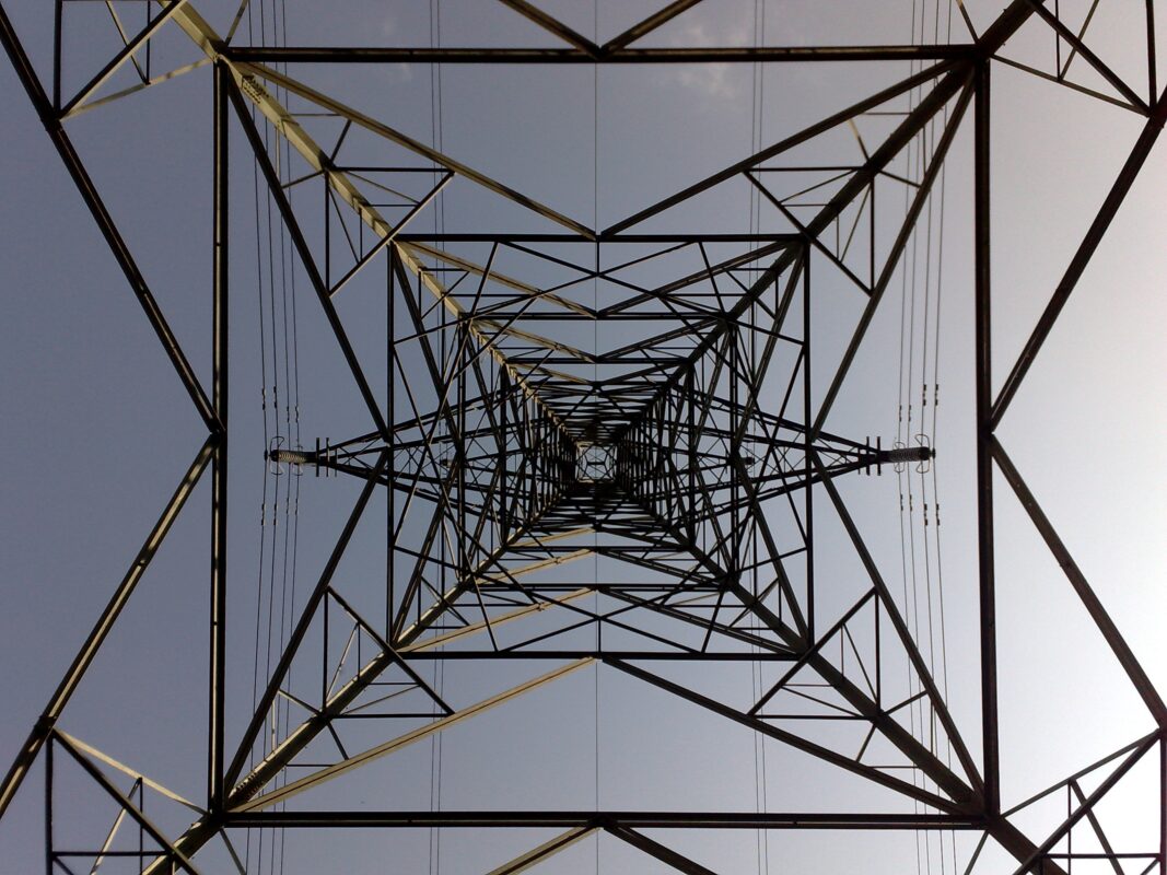 Photo taken from underneath a high tension electricity pylon looking straight up to the apex and showing the symmetrical arrangement of cross braces and upright members