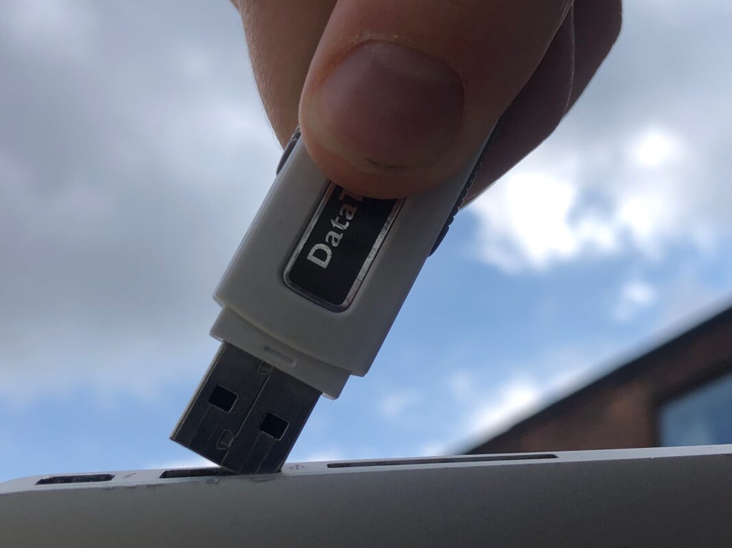 Close-up of a finger inserting a white USB drive labeled 'Data' into a USB port against a cloudy blue sky background